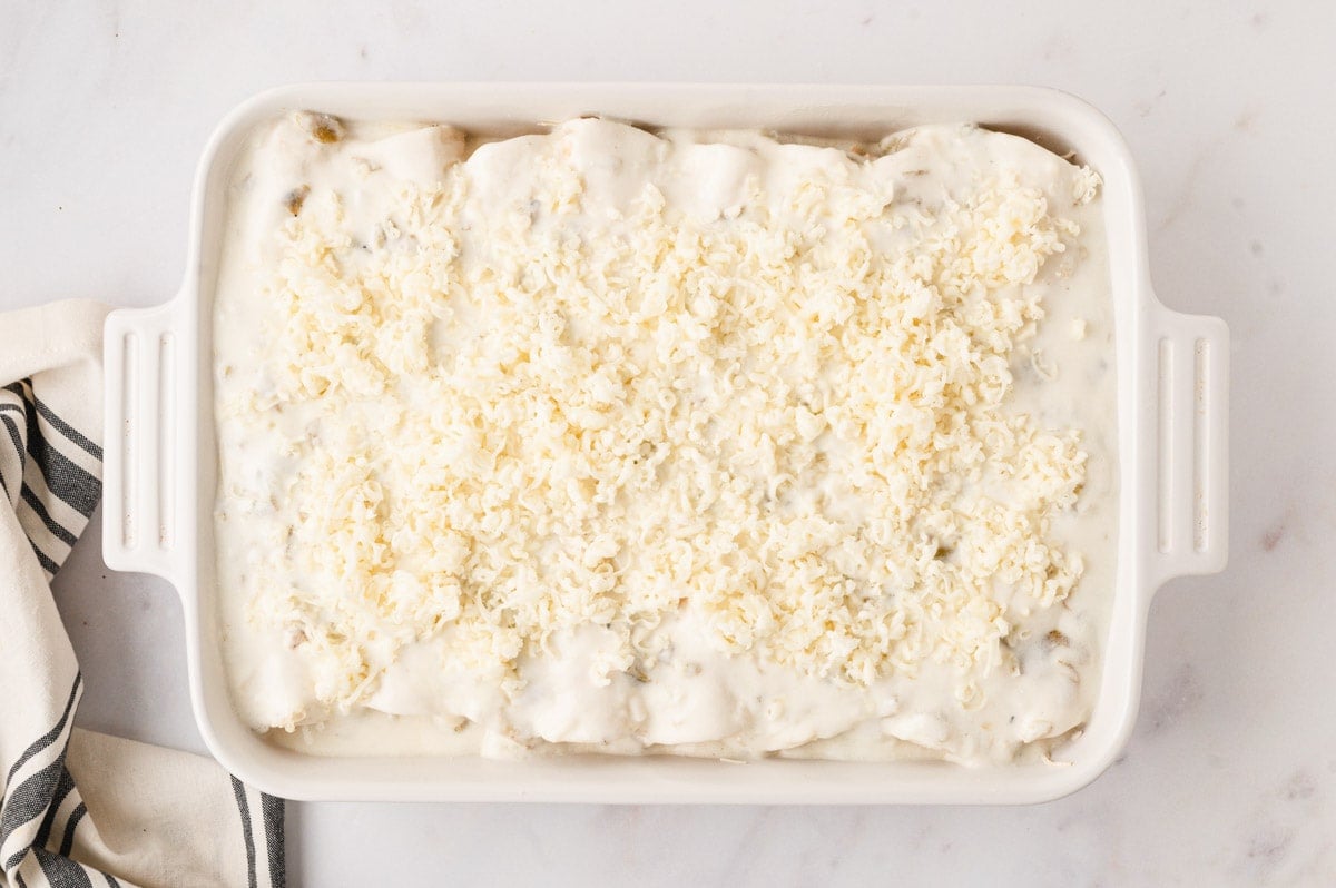 White sauce and cheese over enchiladas in a baking dish.