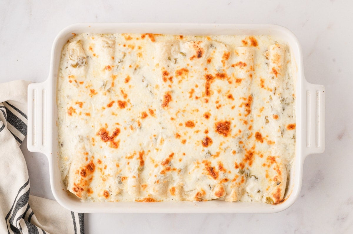 Baked white enchiladas in a baking dish with browned cheese on top.