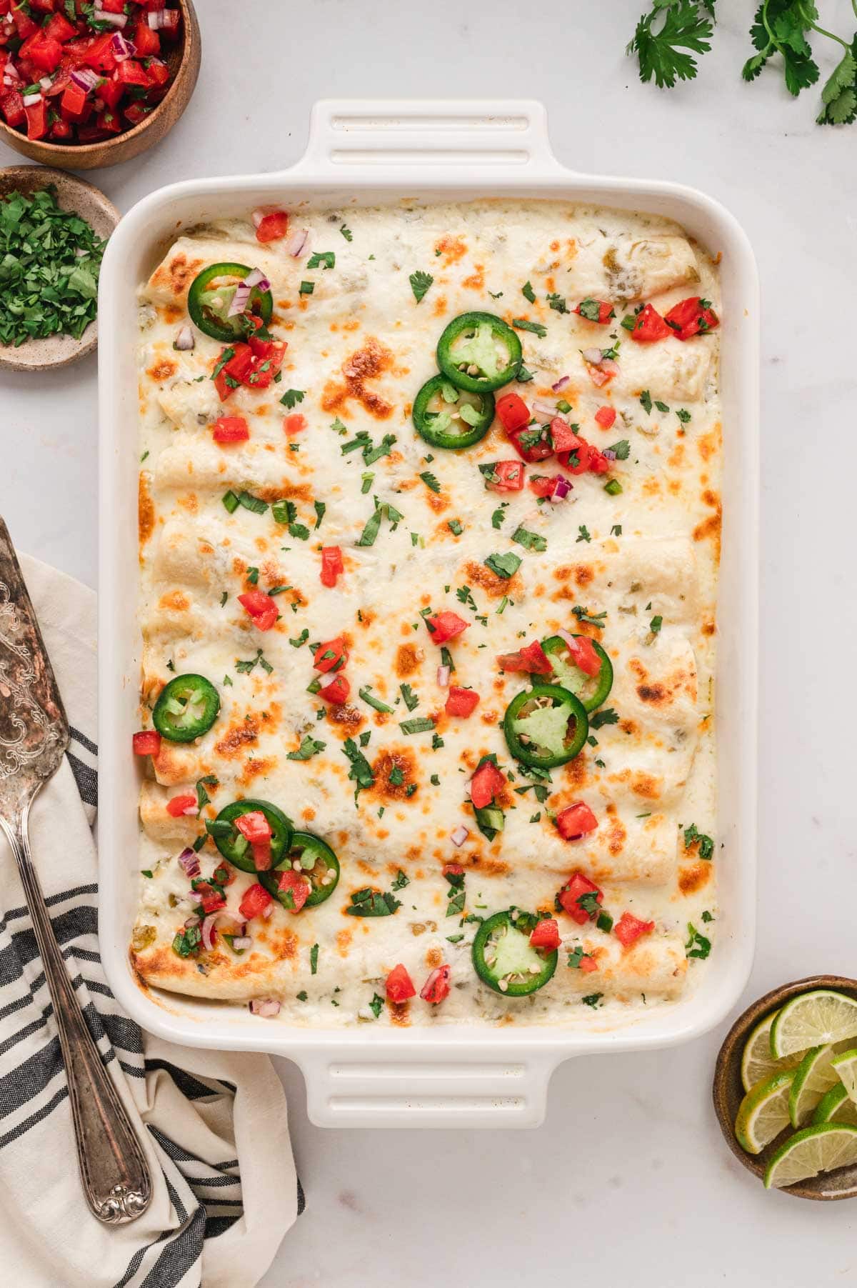 Pan of white enchiladas with diced tomatoes and jalapenos on top.