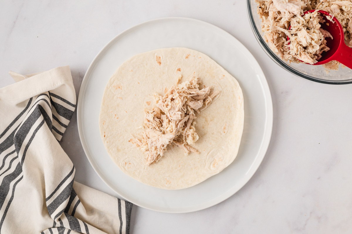 A flour tortilla laid flat on a plate with shredded chicken down the center.
