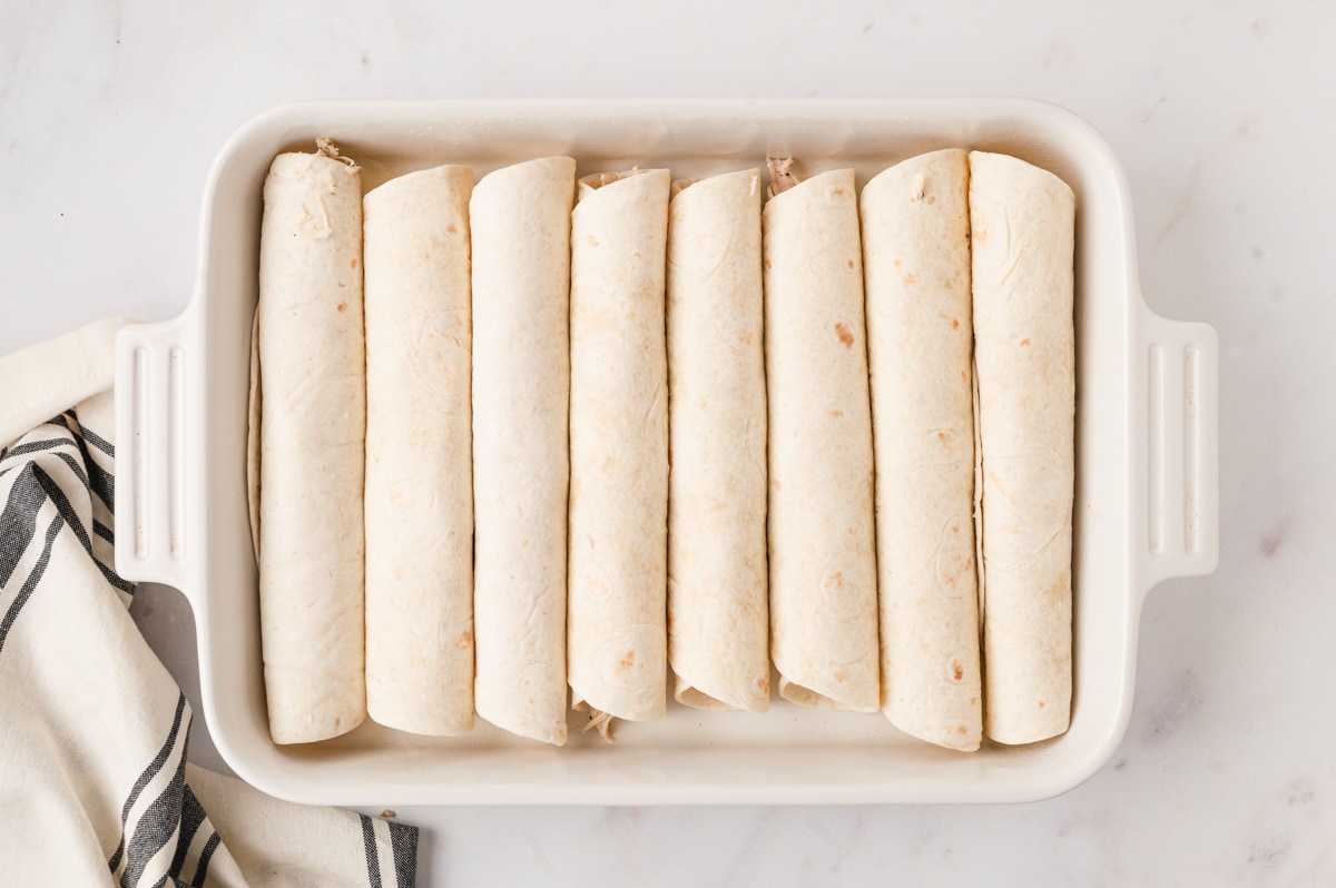 Rolled enchiladas in a baking dish.