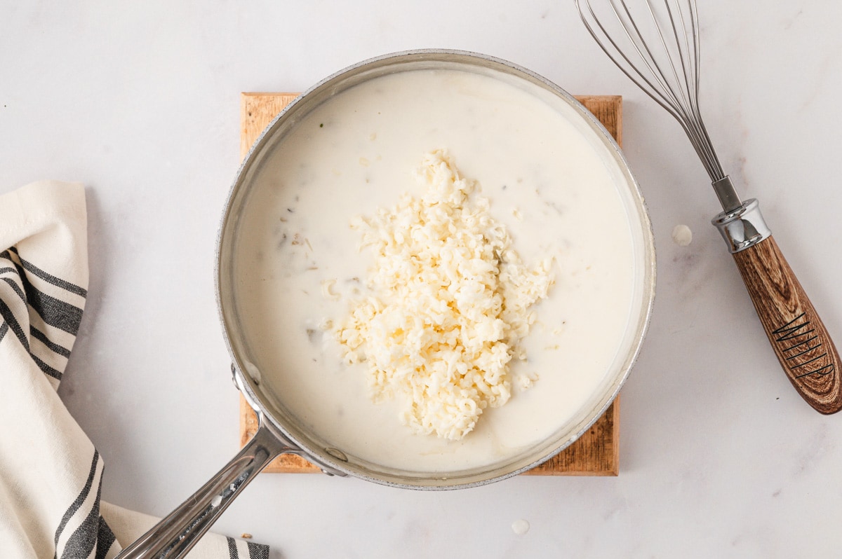 White sauce with shredded cheese in a large pan with a silver handle.