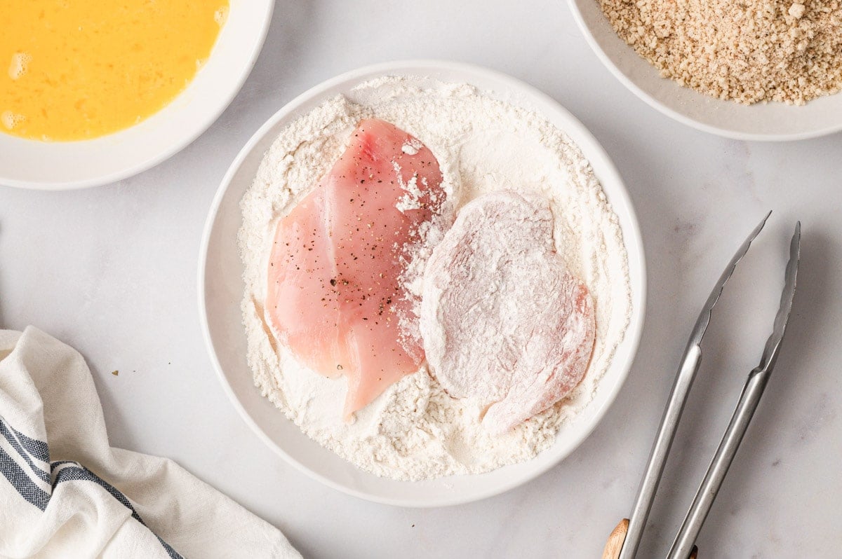 Chicken cutlets in a dish of flour.