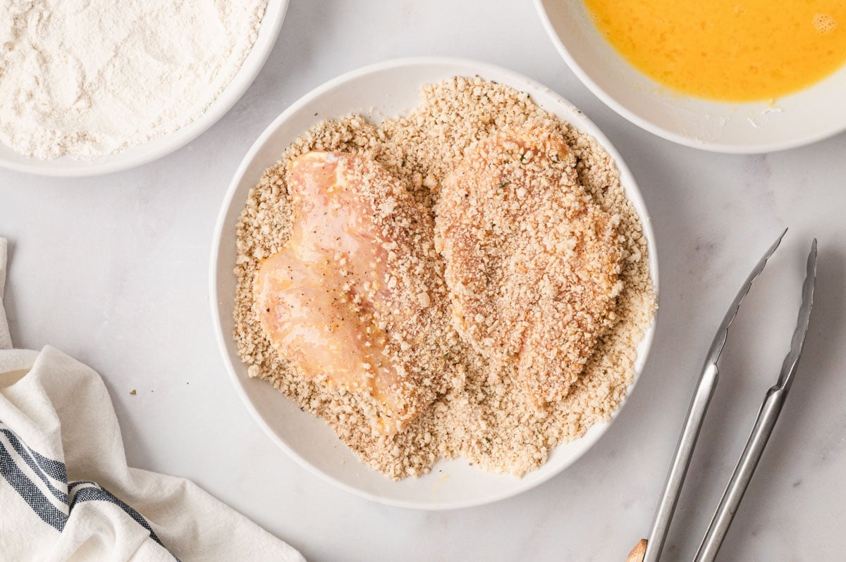 2 chicken cutlets in a dish of panko breadcrumbs.