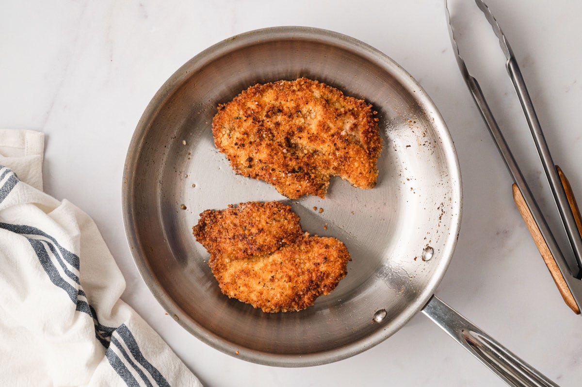 2 chicken cutlets, breaded and fried in a skillet.