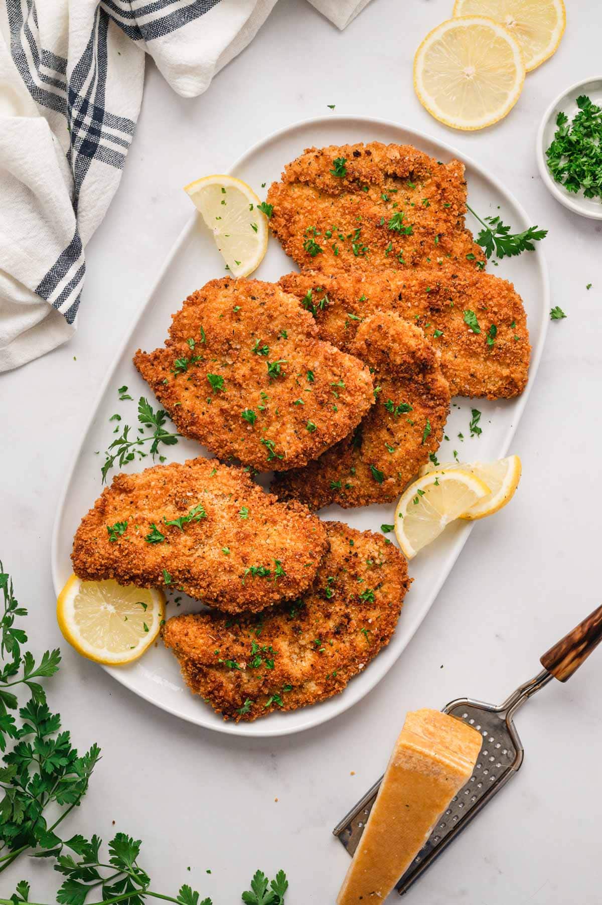 5 breaded chicken cutlets on a white serving platter.