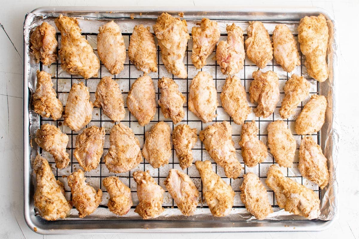 buffalo chicken wings coated with flour and spices on a baking rack over a baking sheet