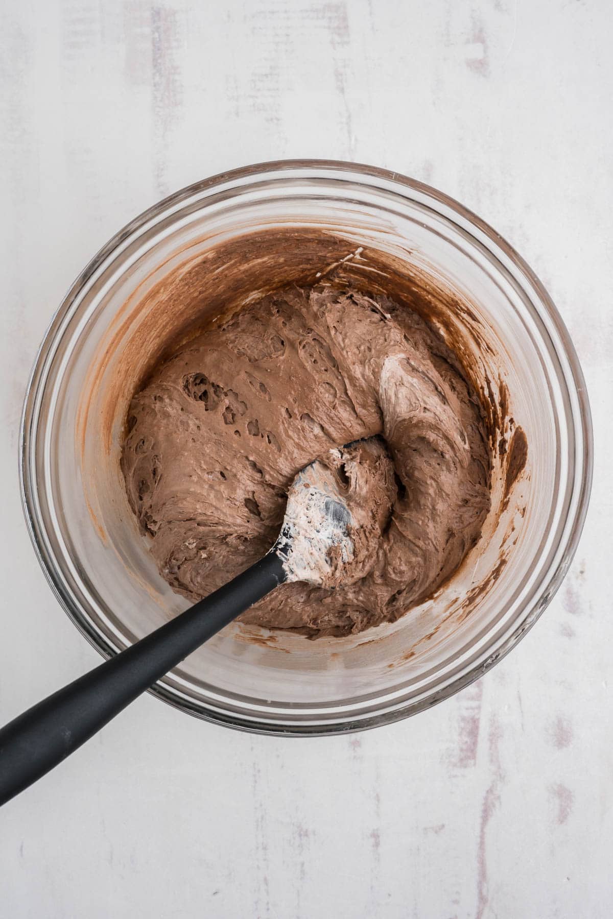 Cookie dough in a clear glass bowl with a mixing spoon.