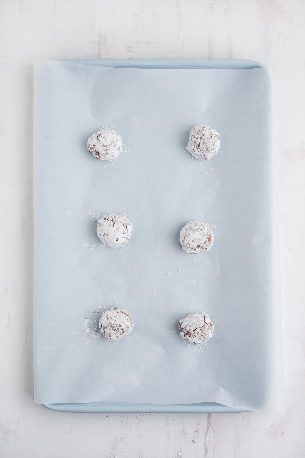 Cookie dough balls covered ni powdered sugar and sitting on a parchment paper covered cookie sheet. 