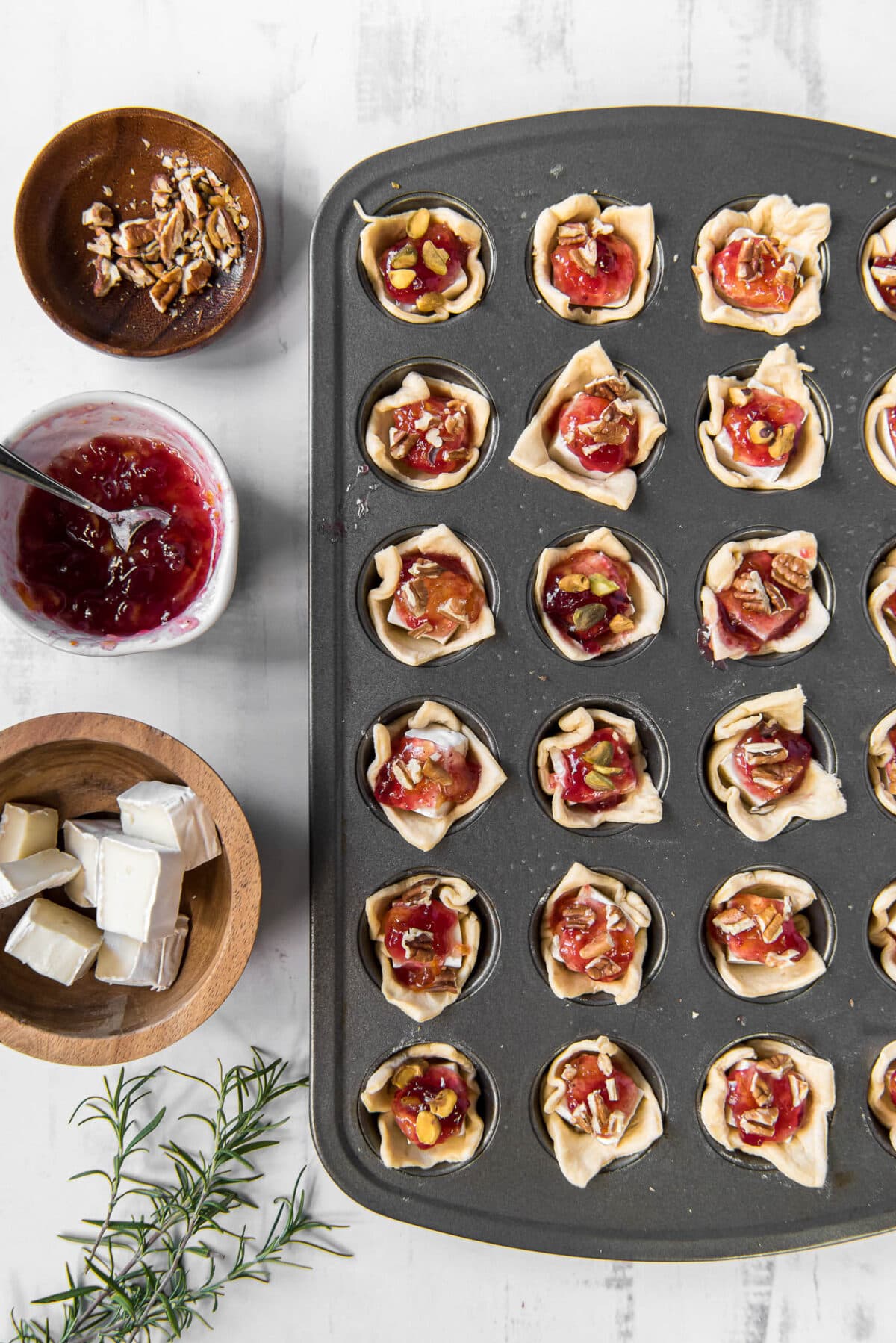 Crescent dough in muffin cups with brie cheese topped with cranberry sauce and pistachios.