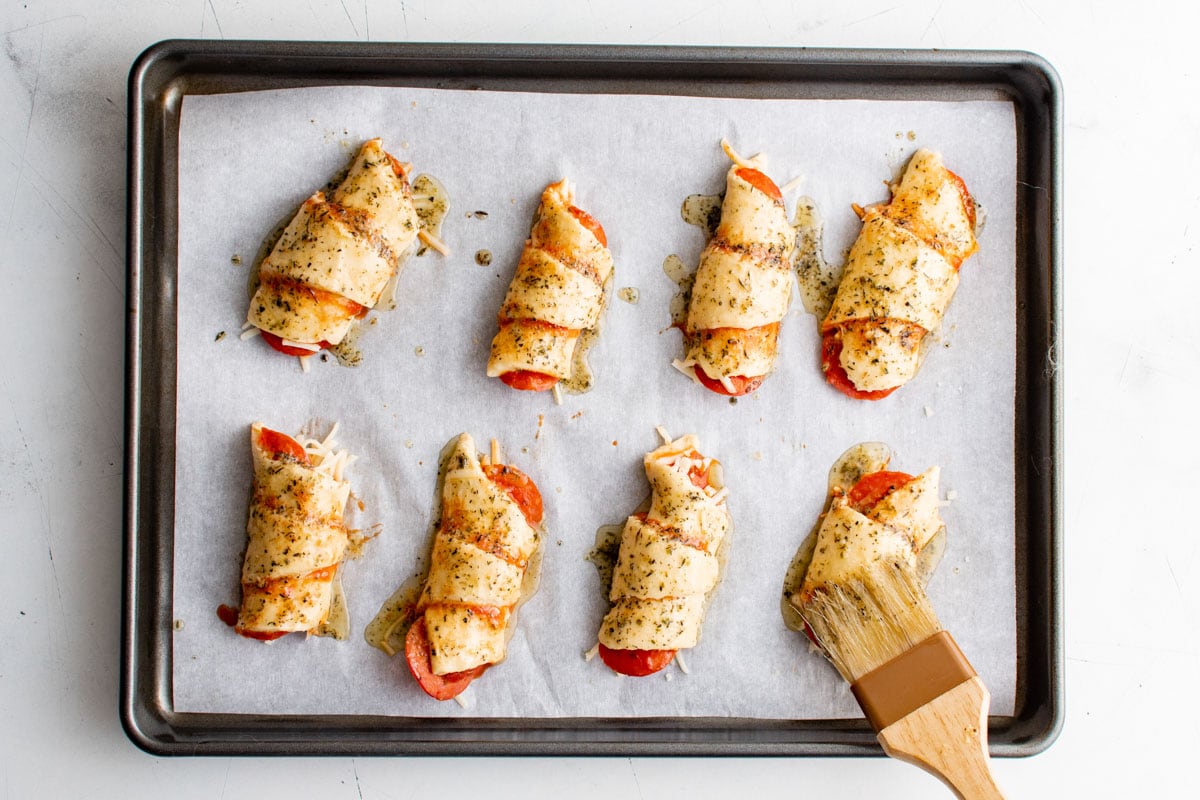 Crescent roll pizza inspired on a baking tray with a pastry brush brushing butter on them.