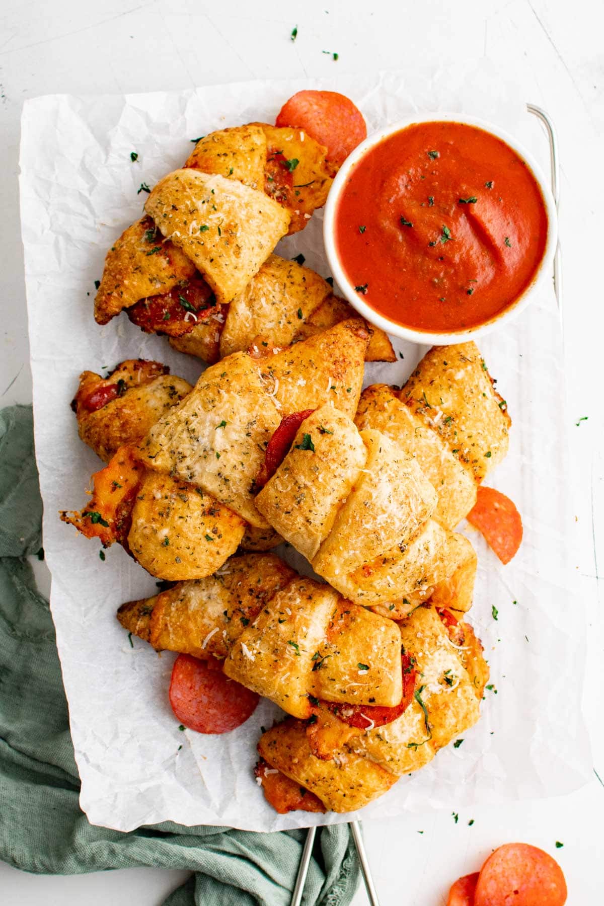 Pile of crescent rolls with pepperoni, italian seasoning and a dish of marinara sauce.