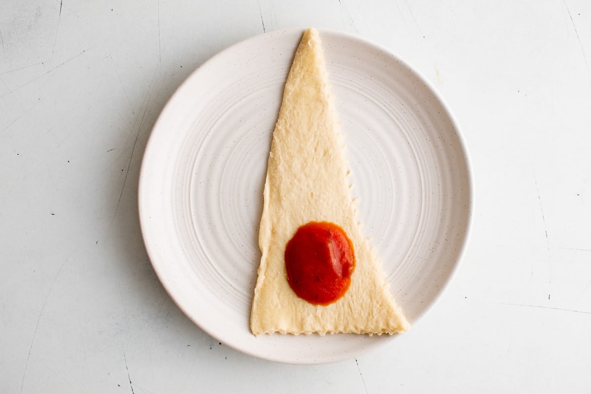 Crescent roll triangle with a blob of pizza sauce. On a white plate.