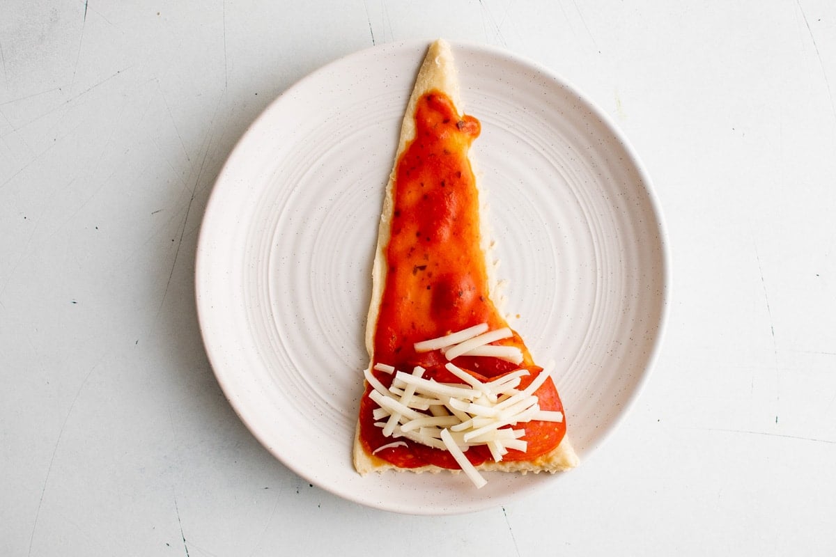 Crescent roll triangle with pizza sauce and pepperoni and shredded mozzarella cheese.