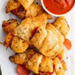 Pile of crescent rolls with pepperoni, italian seasoning and marinara sauce.