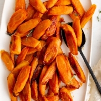 Roasted carrots on a white serving platter with a black serving spoon.
