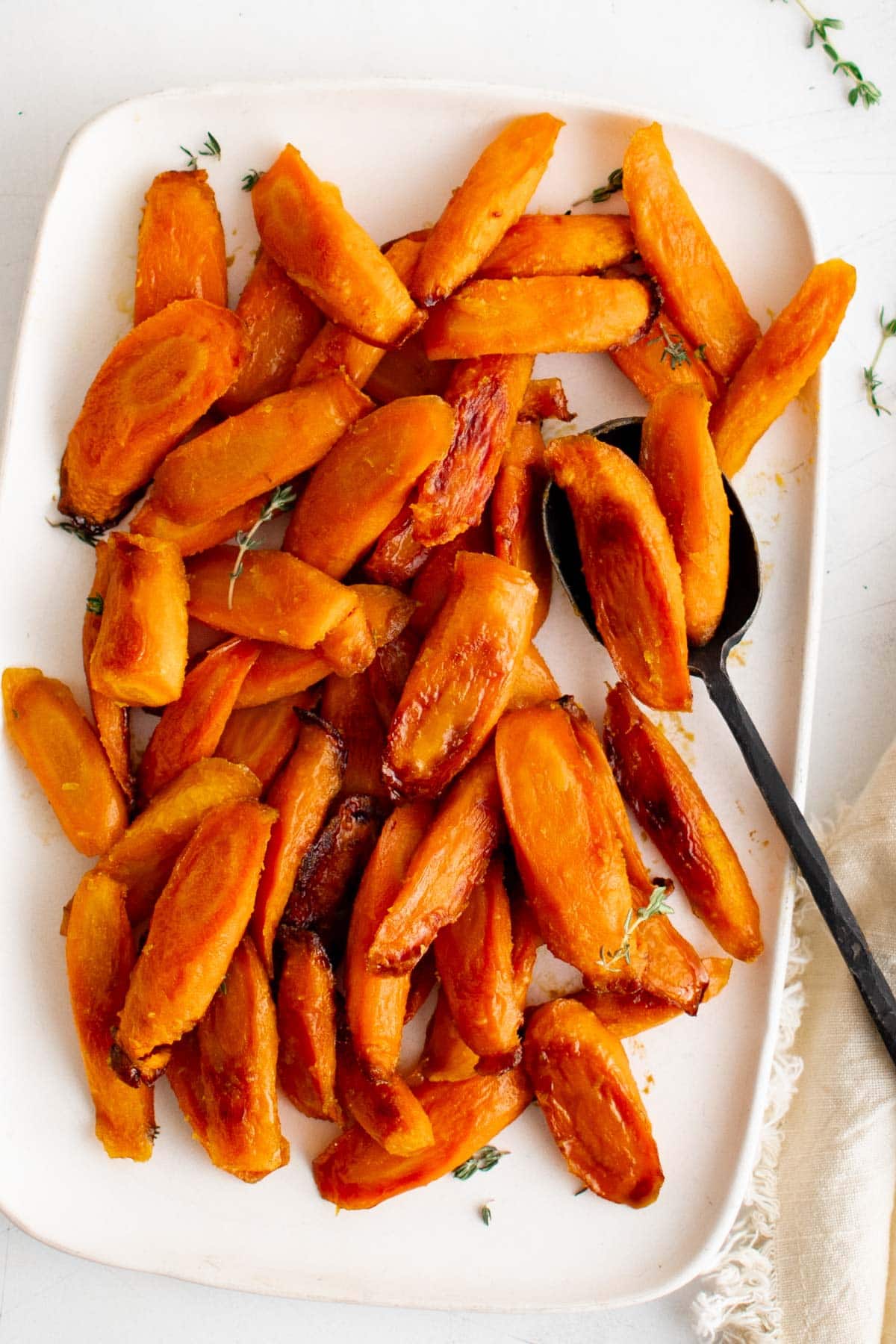 Roasted carrots on a white serving platter with a black serving spoon. 