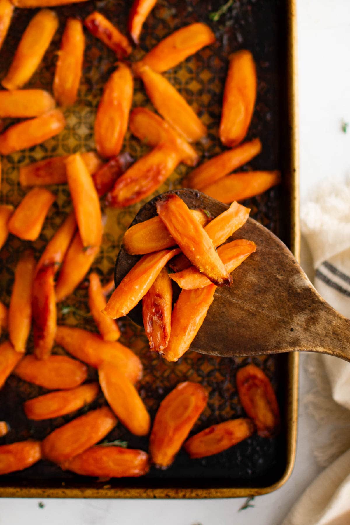 Roasted carrots on a baking sheet with a wooden spatula.