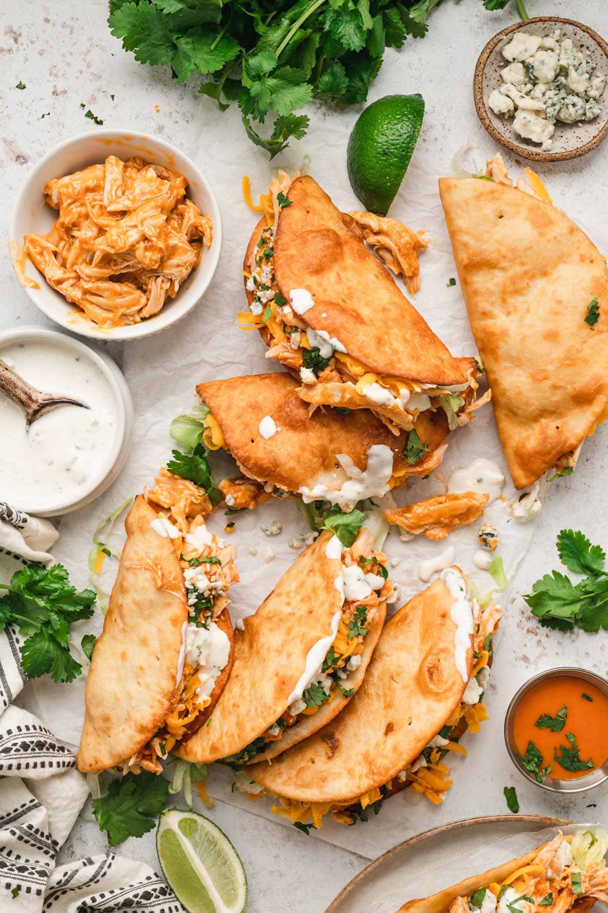 Buffalo chicken tacos with blue cheese, lettuce and cilantro, laying on a white surface.