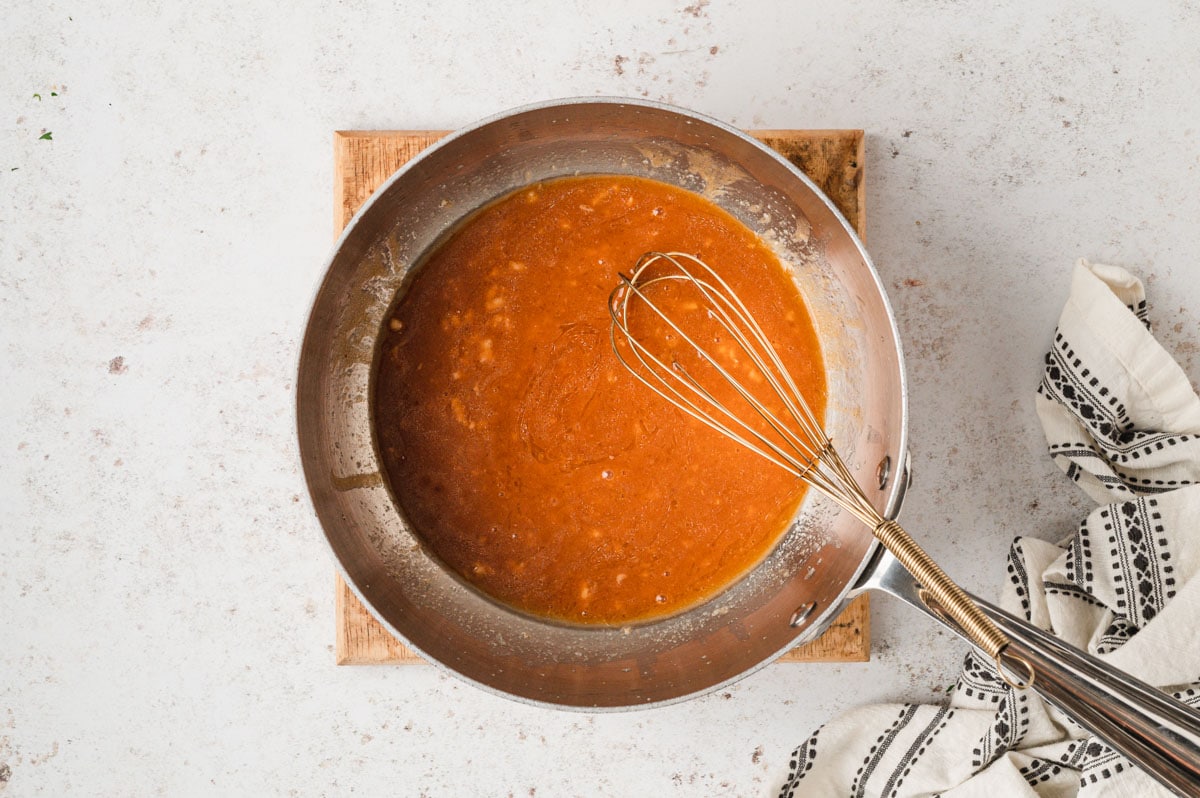 Buffalo sauce a a whisk in a metal skillet.