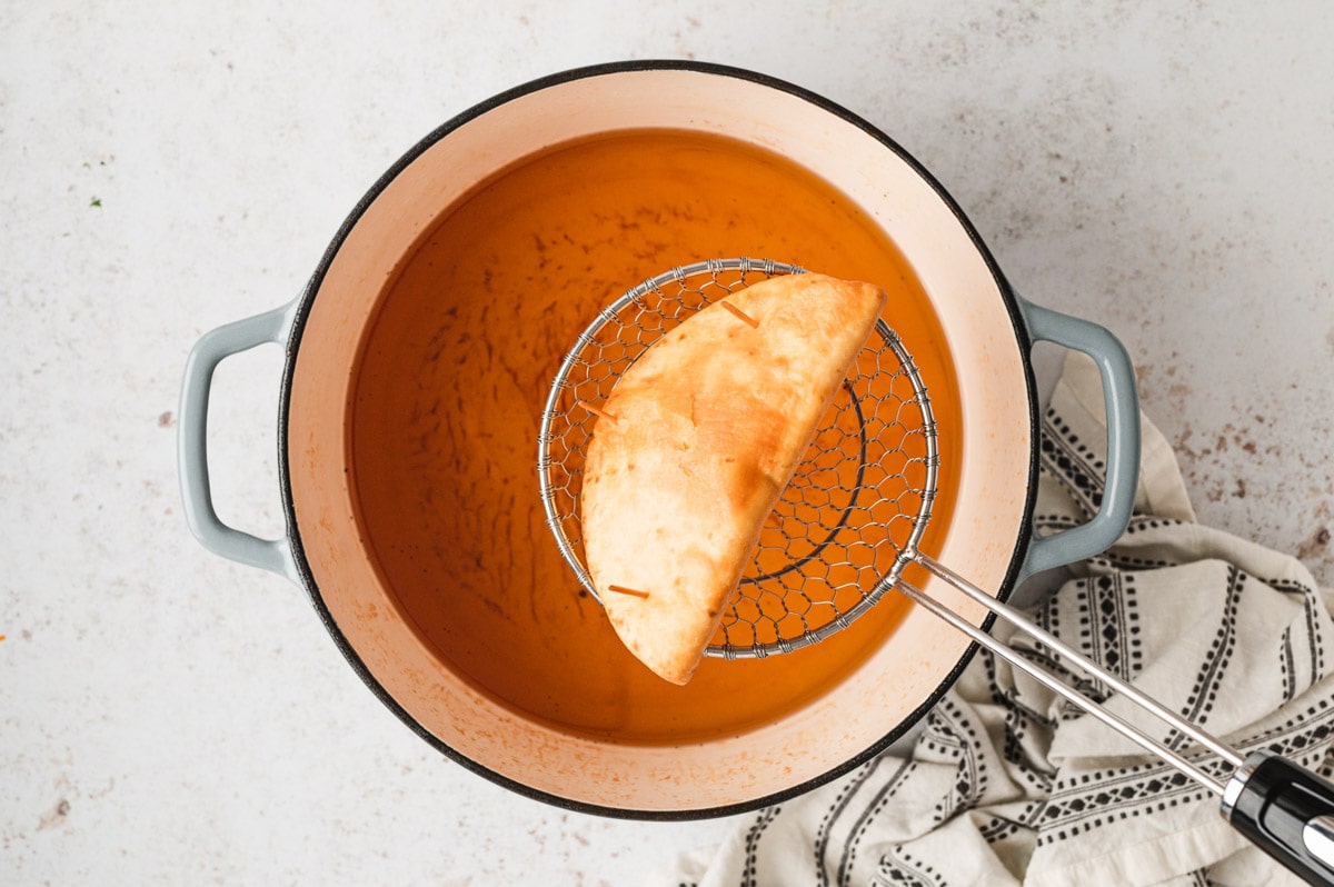 Crispy fried flour tortilla taco shell in a metal strainer spoon over a large pot of frying oil.