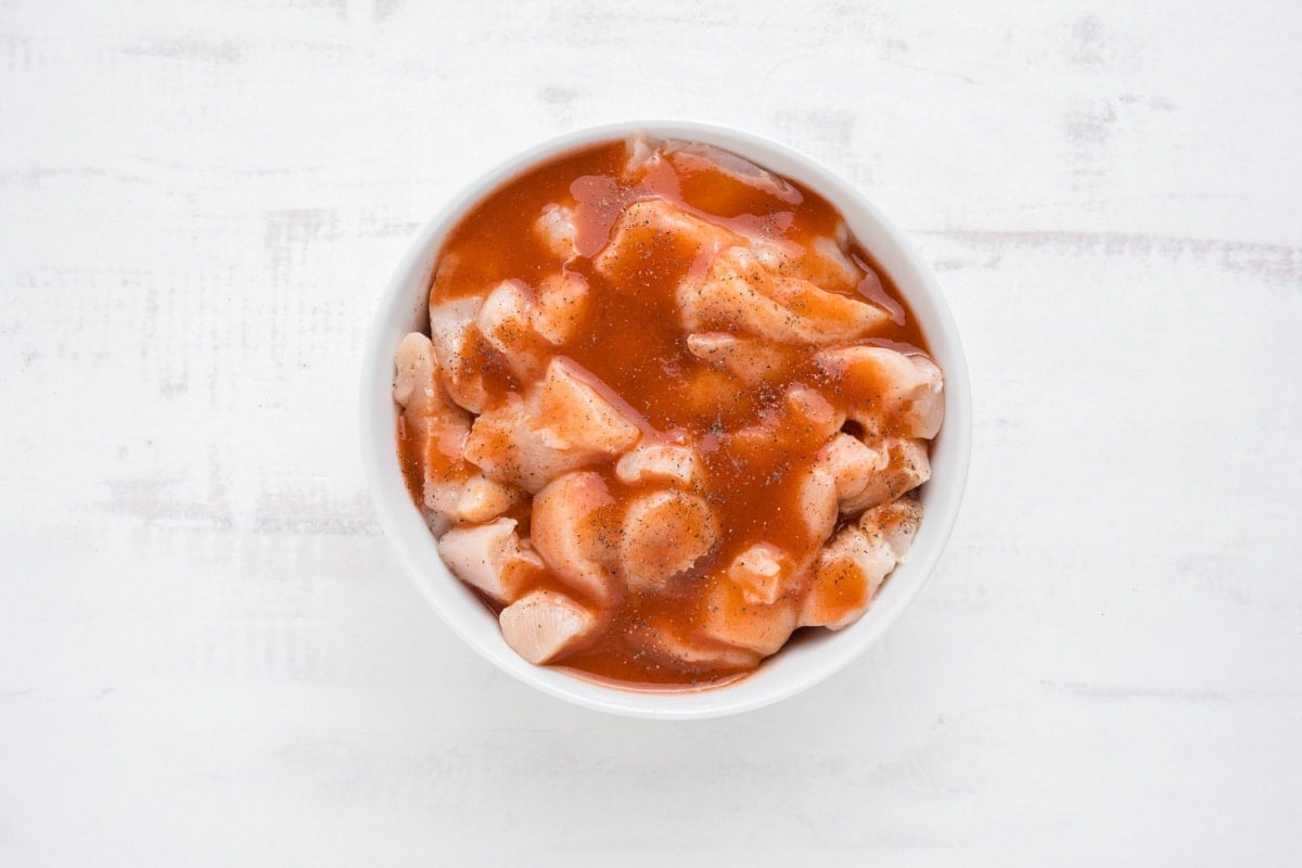 Chicken breast pieces in buffalo sauce in a bowl.