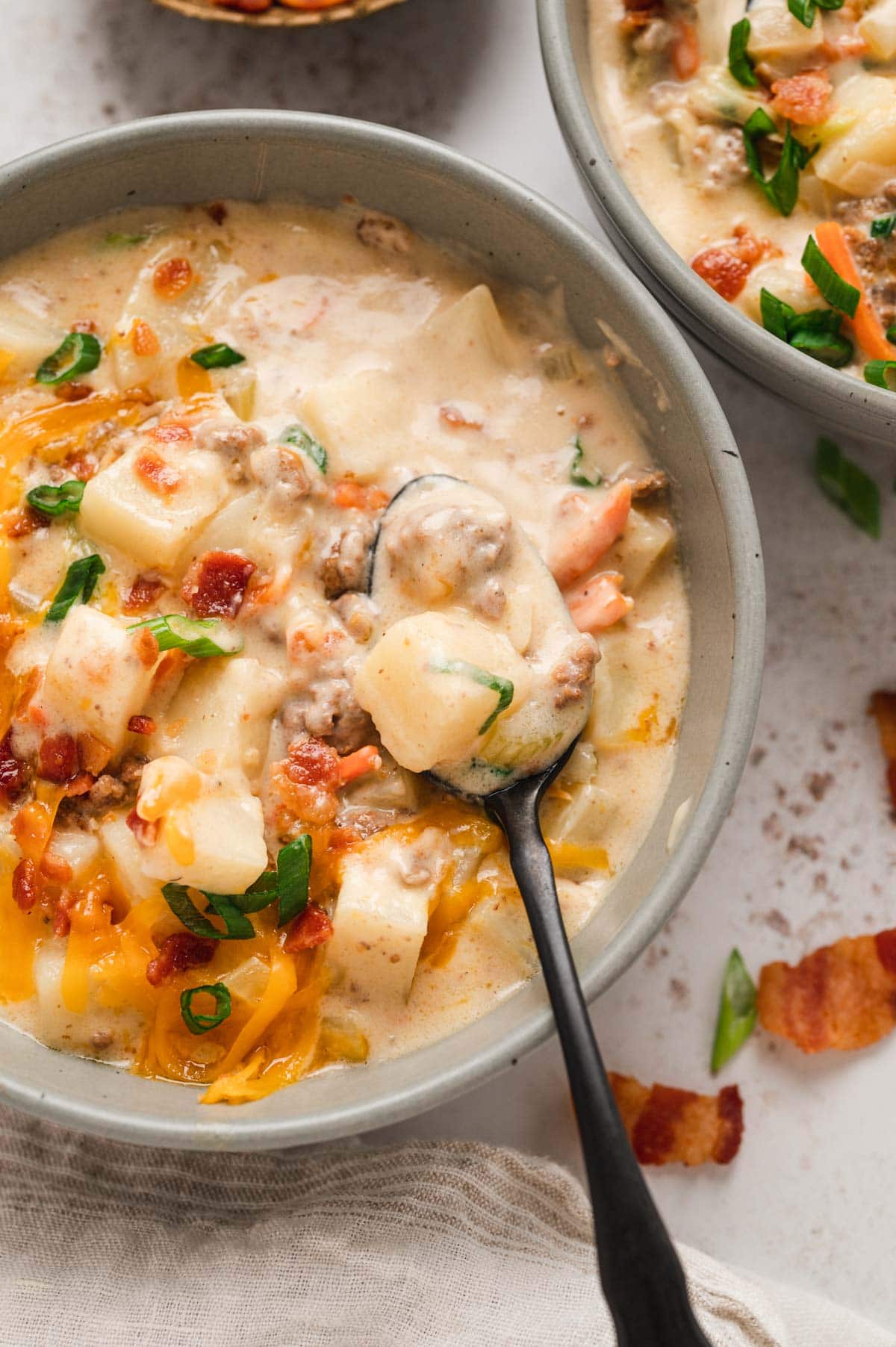 Gray bowl with cheeseburger soup with shredded cheese, potatoes and green onions and bacon.