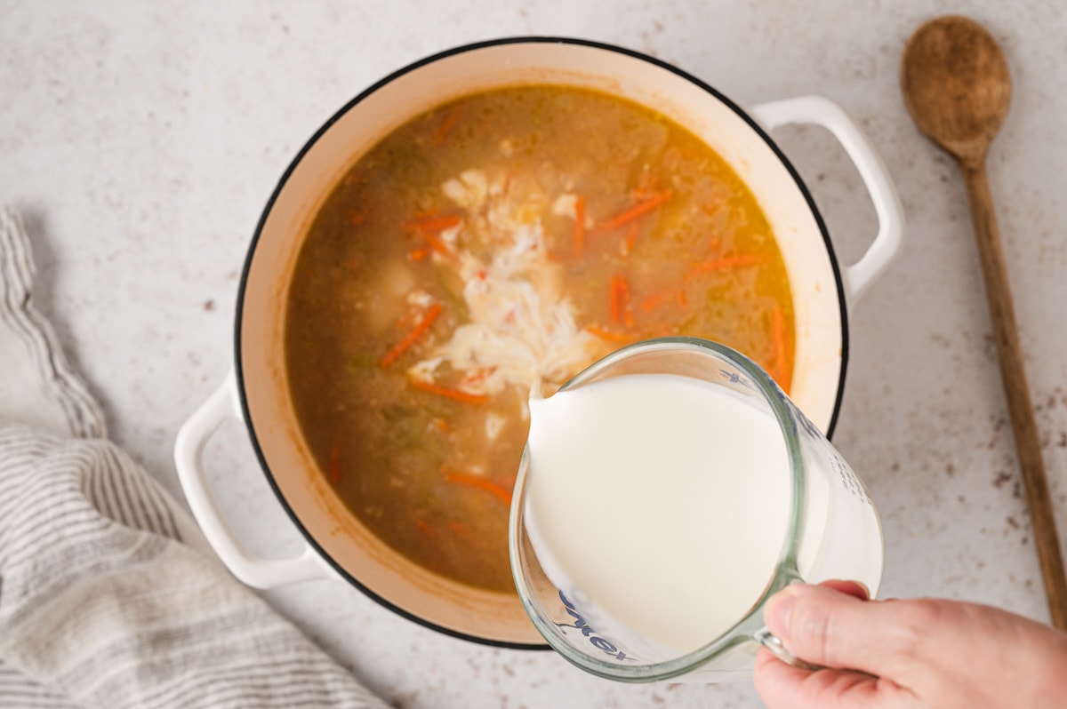 pouring cream from a glass measuring cup in to a pot of broth.