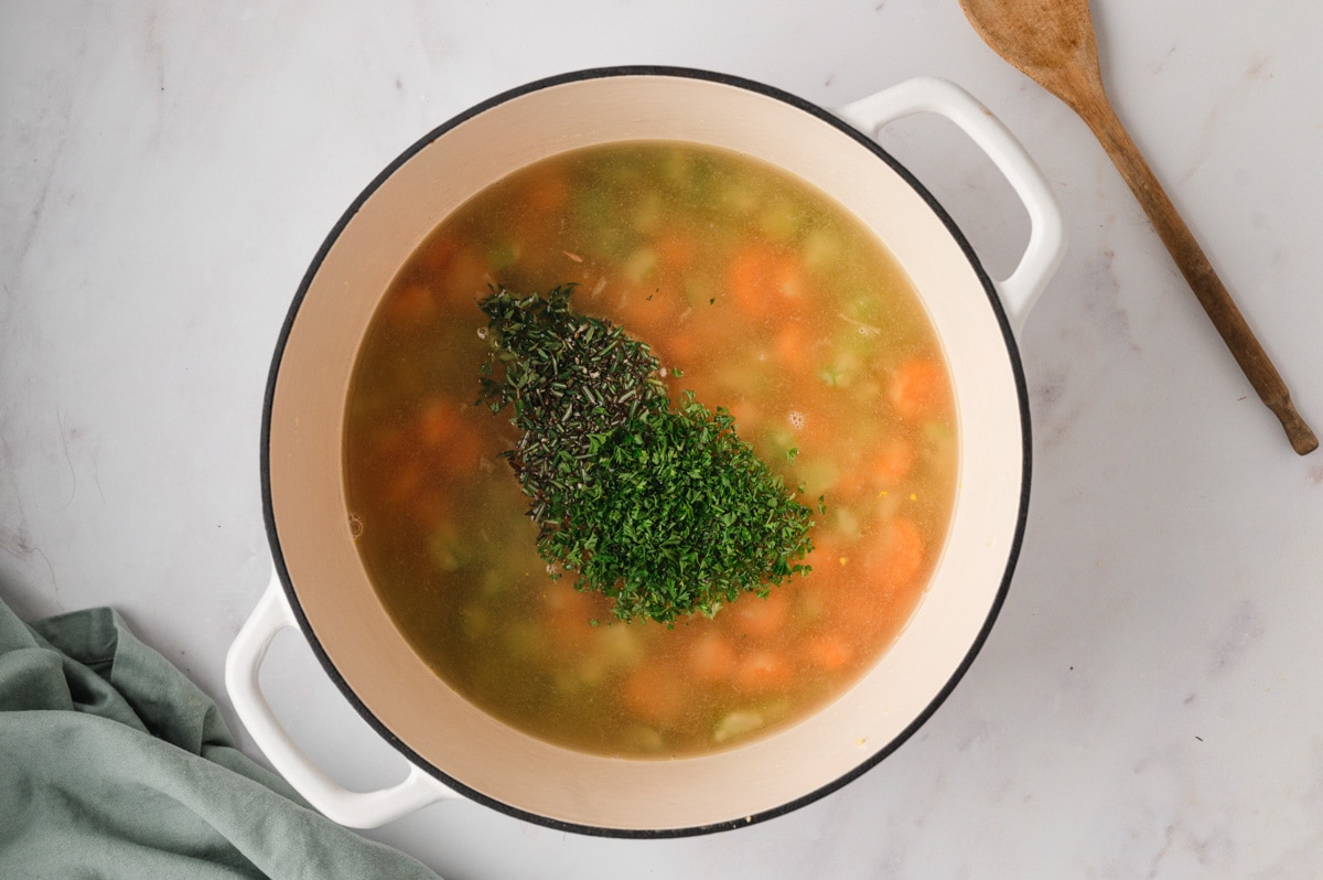 Chopped herbs added to a pot of broth and vegetables.