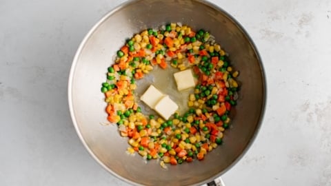 Diced carrots, corn and peas with 3 pats of butter in a wok.