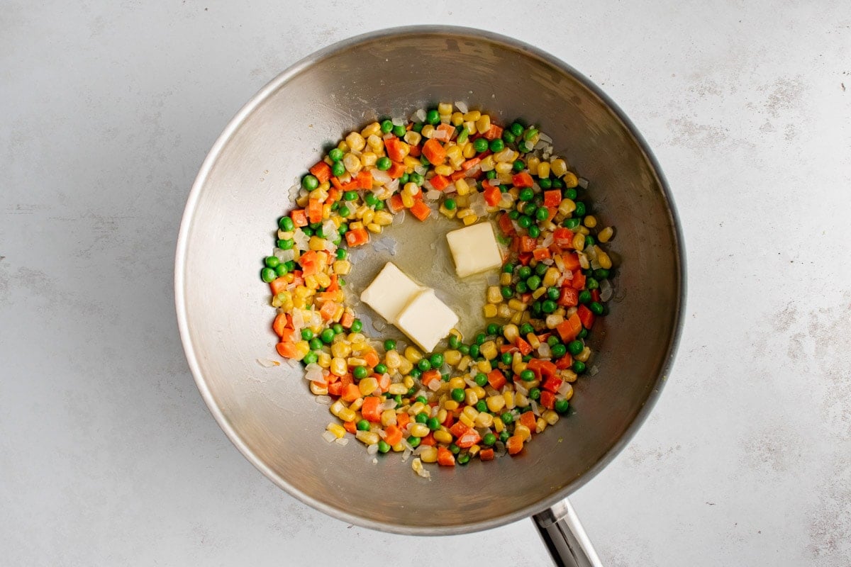 Diced carrots, corn and peas with 3 pats of butter in a wok.