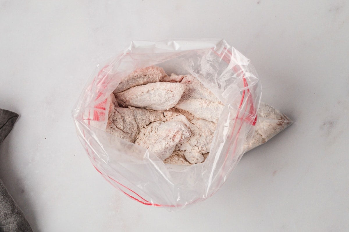 Chicken wings coated in flour in a plastic bag.