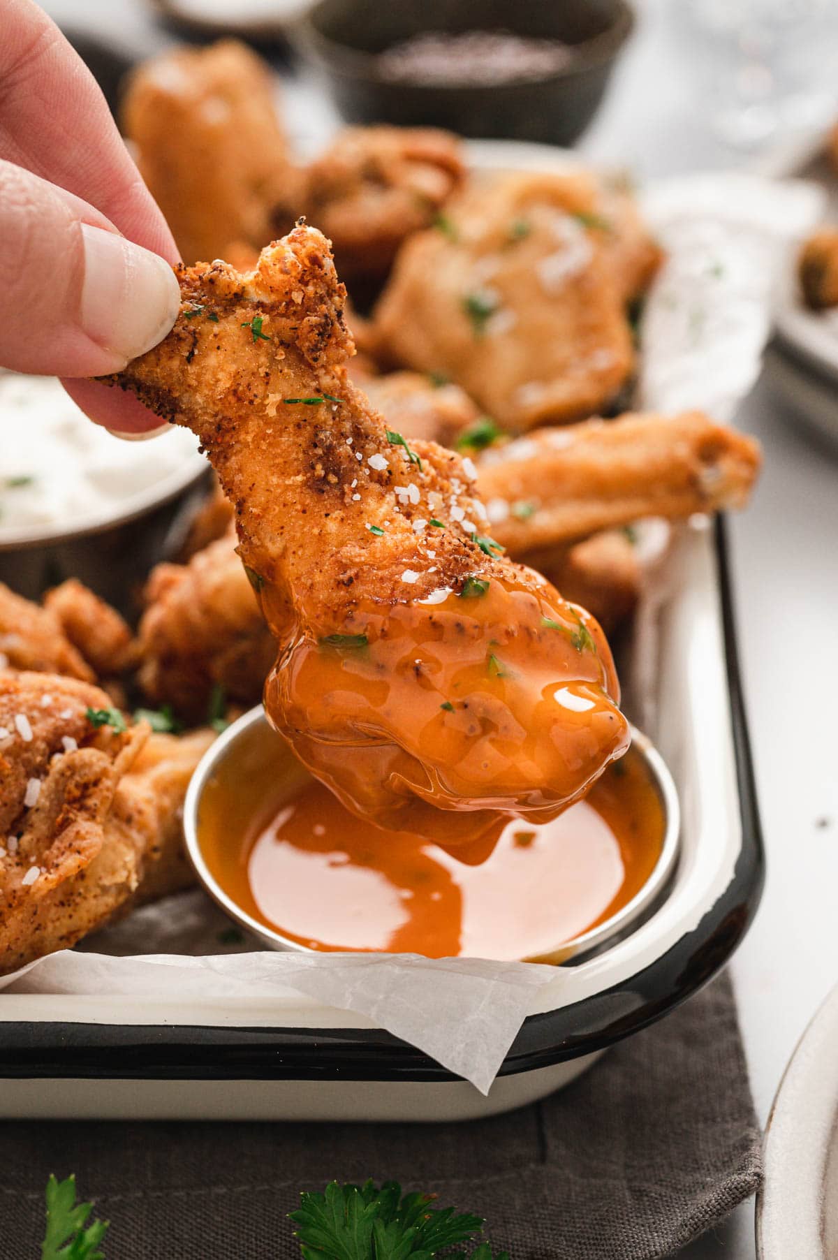 A hand dipping a chicken wings in a buffalo sauce.