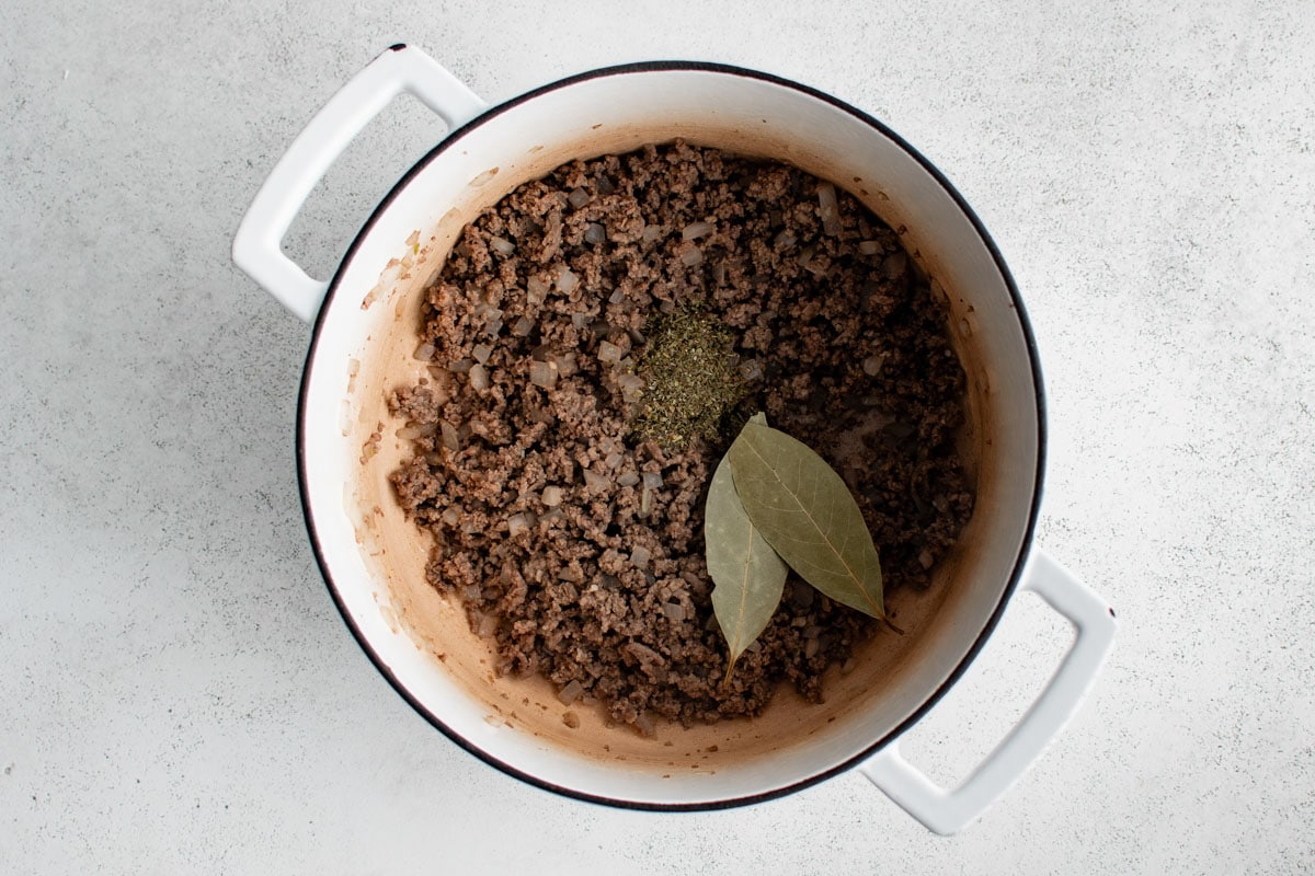 Ground beef in a pot with bay leaves.