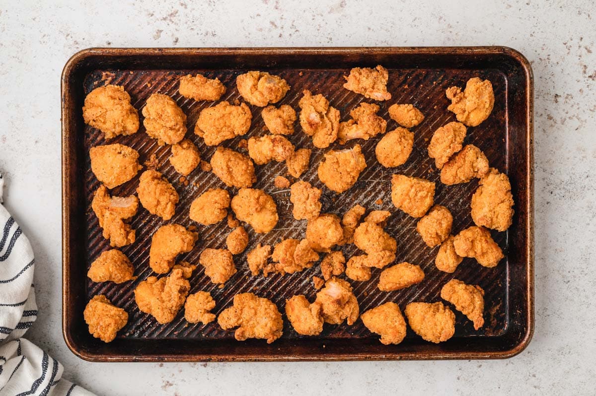 Popcorn chicken spread out on a baking sheet.