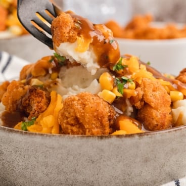 Fork taking a pieces of popcorn chicken from a mashed potato bowl.