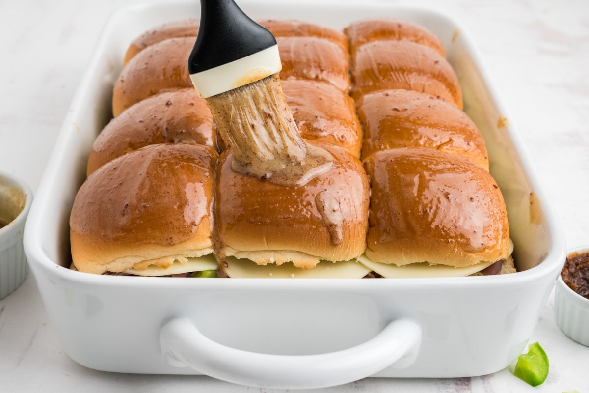 Rolls in a baking dish and a pastry brush brushing with melted butter.