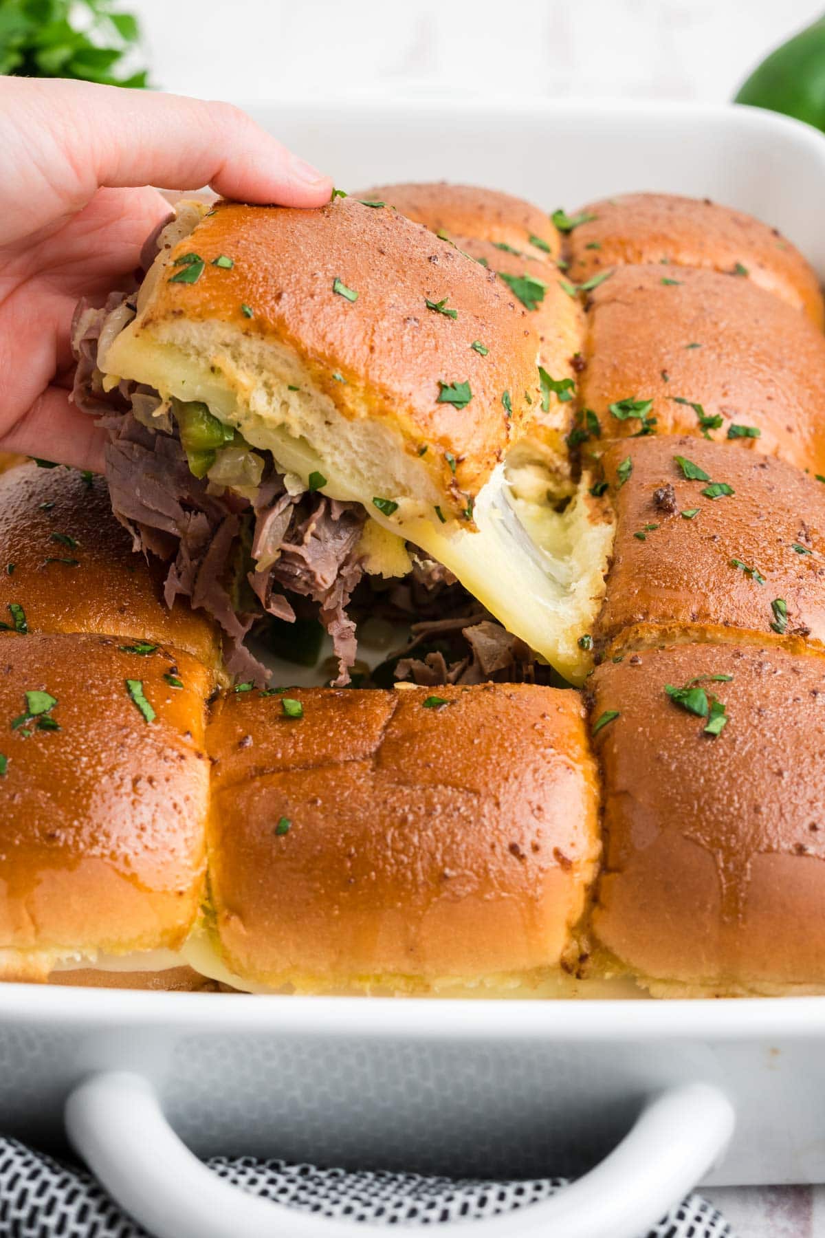 Philly cheesesteak slider being pulled from a plate of sliders.