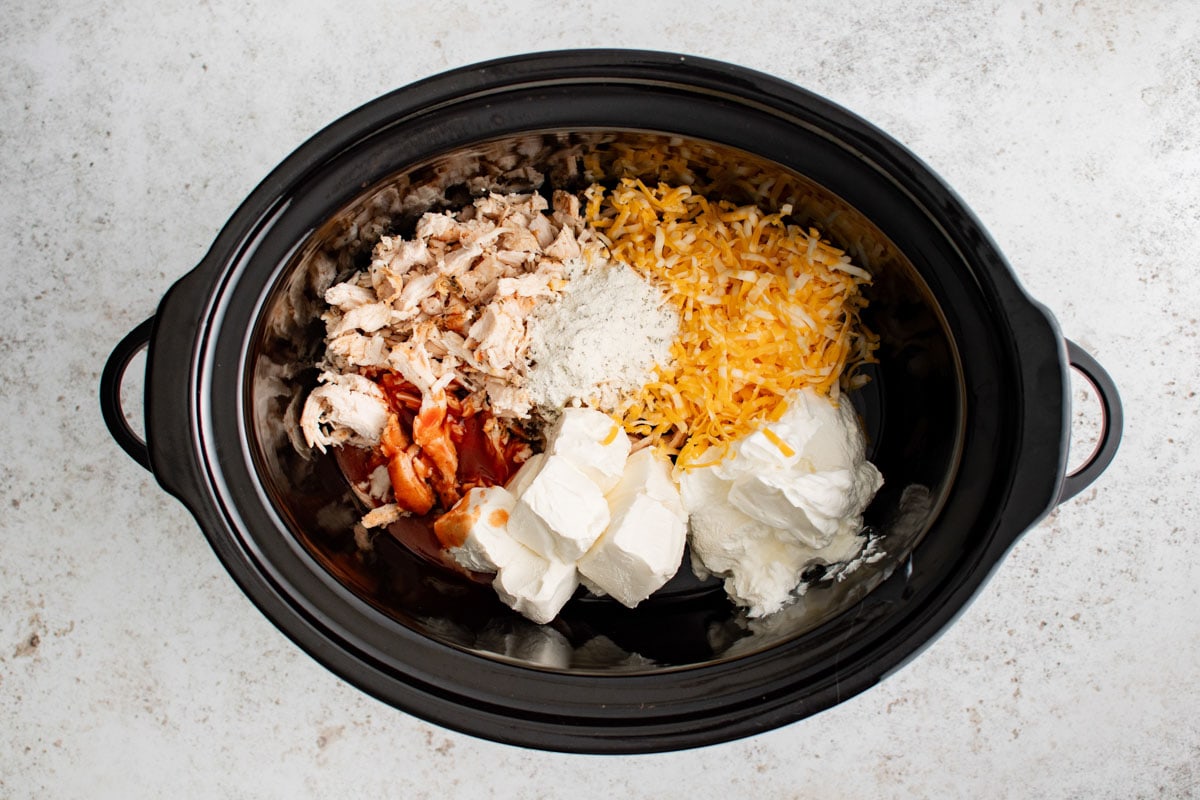Crock pot with cream cheese, buffalo sauce, cheese and chicken.