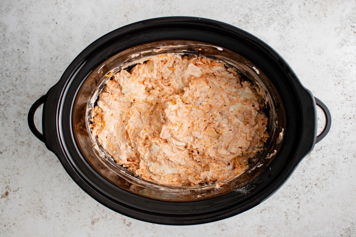 Light orangey-pink cream cheese mixture in a slow cooker.