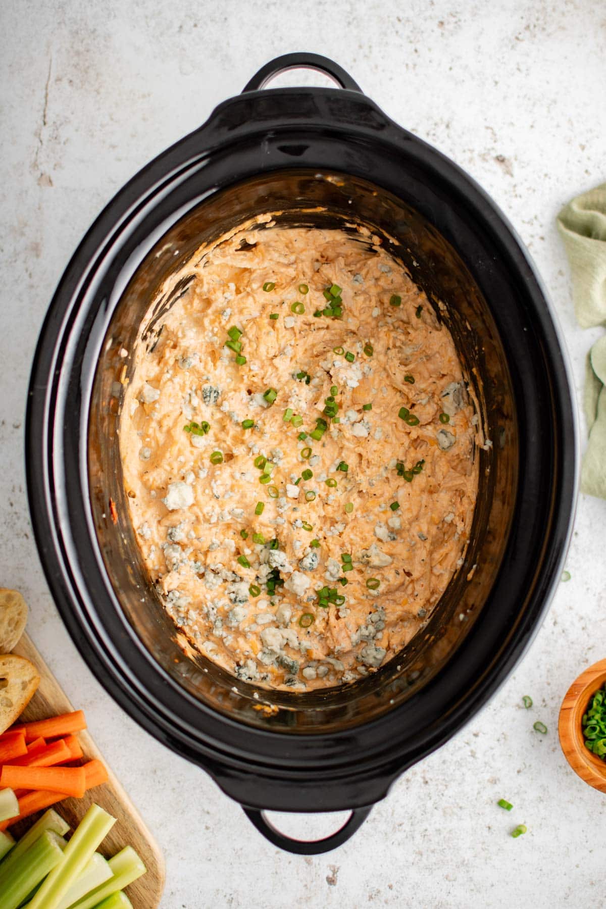 Slow Cooker Buffalo Chicken Dip with blue chese and green onion garnish, in a black crock pot.