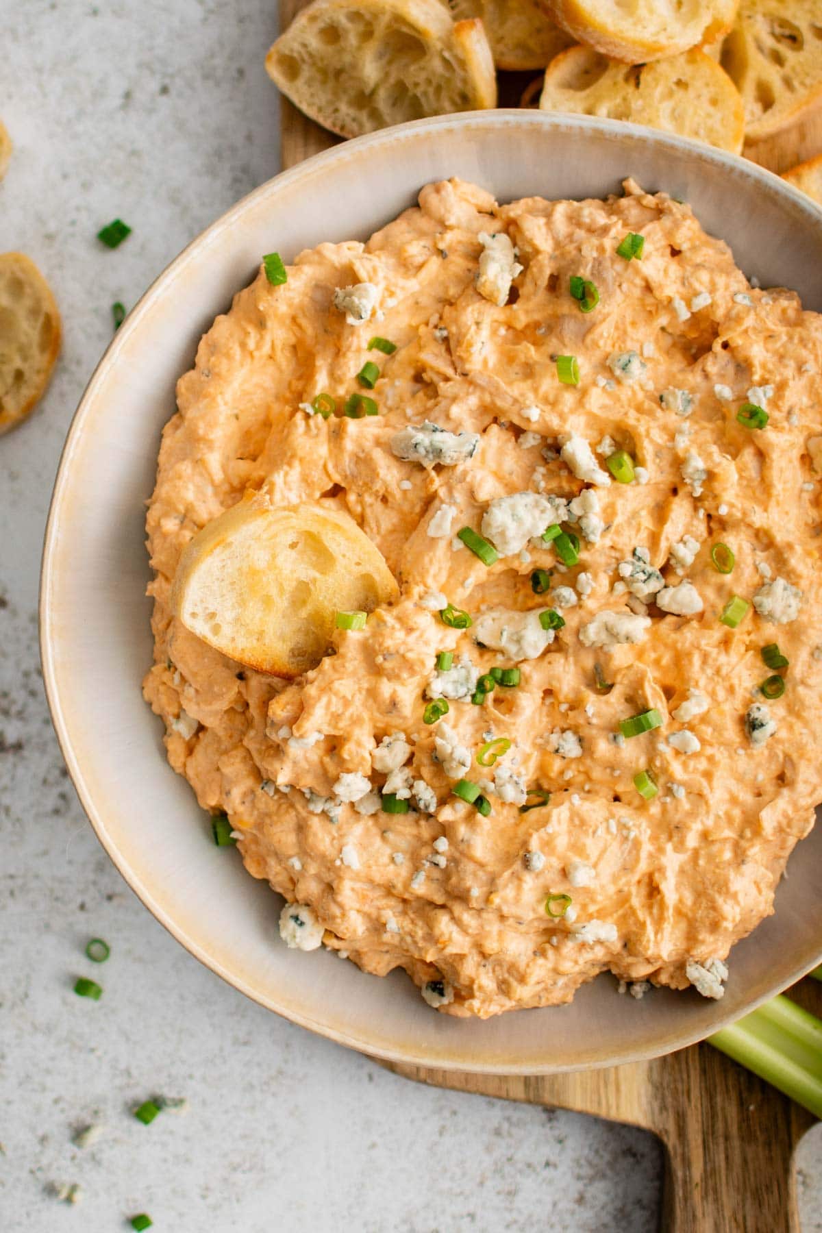 Buffalo chicken dip in a white serving bowl with a piece of bread and blue cheese.