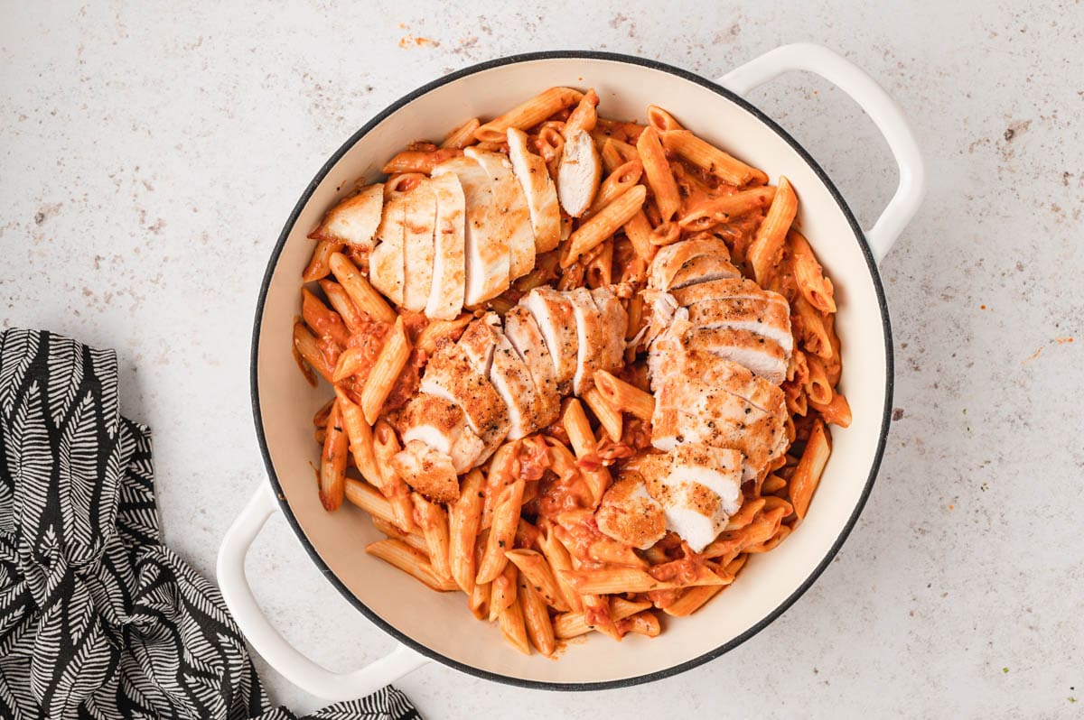 Penne pasta and sliced chicken in a red sauce in a skillet.