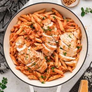 Penne pasta, chicken in a red sauce in a white skillet.