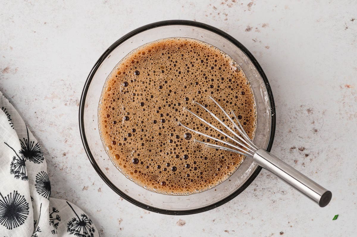 Brown sauce in a clear glass bowl with a small whisk.