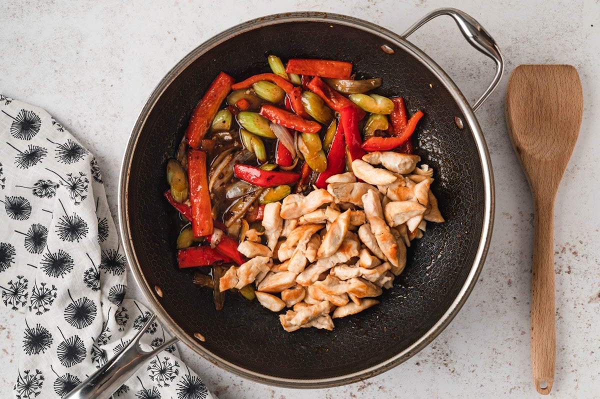 Chicken breast pieces, red bell pepper, onion and celery slices in a skillet.