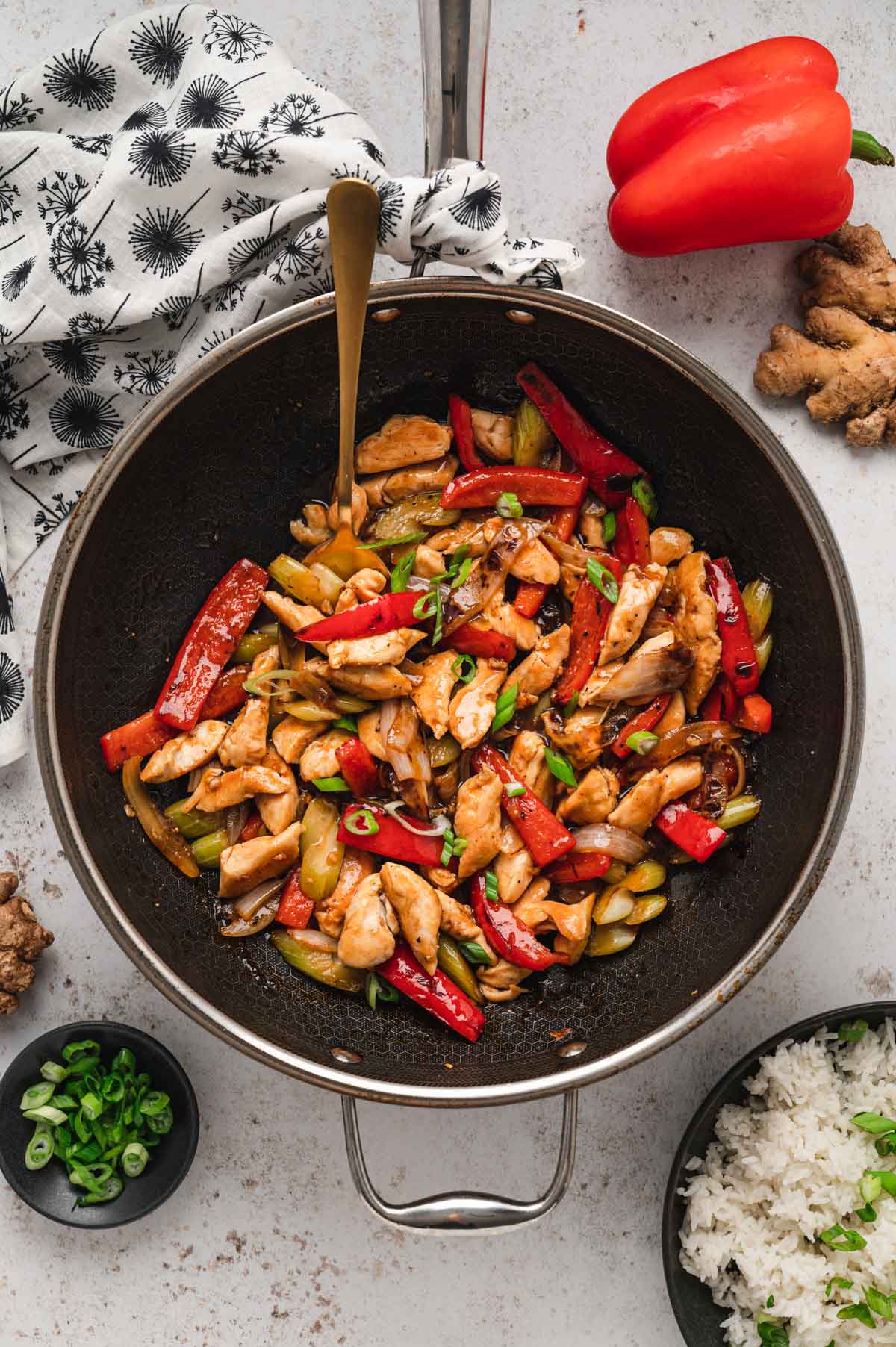 Black pepper chicken with bell peppers, onion and celery in a skillet with a spoon.