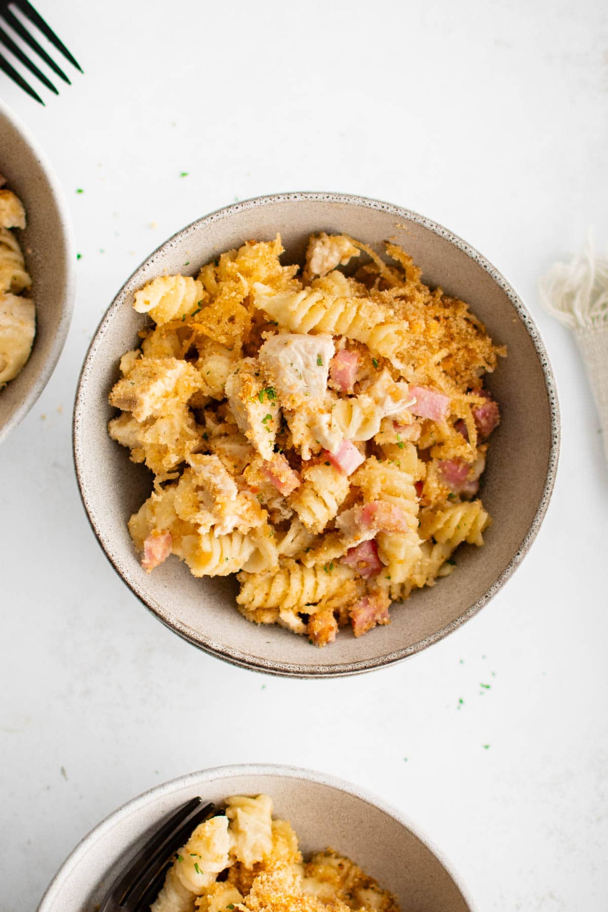 Small serving bowl with rotini pasta, cheese sauce, ham and chicken and a breadcrumb topping.