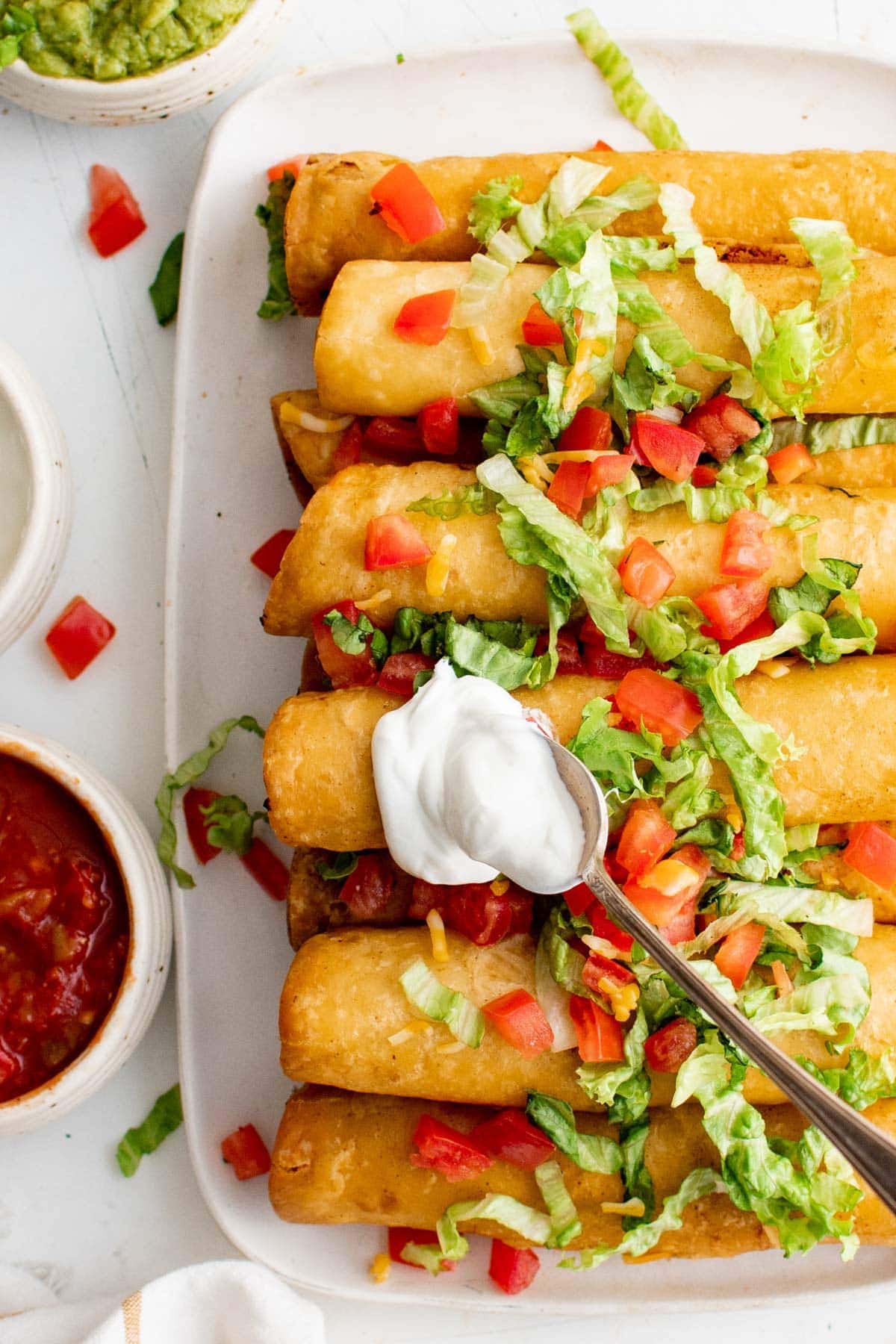 platter of flautas with shredded lettuce, diced tomatoes and sour cream