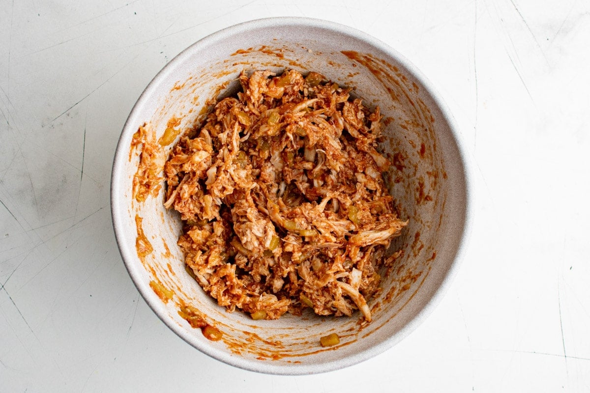 Shredded chicken mixed with tomato sauce in a large bowl.